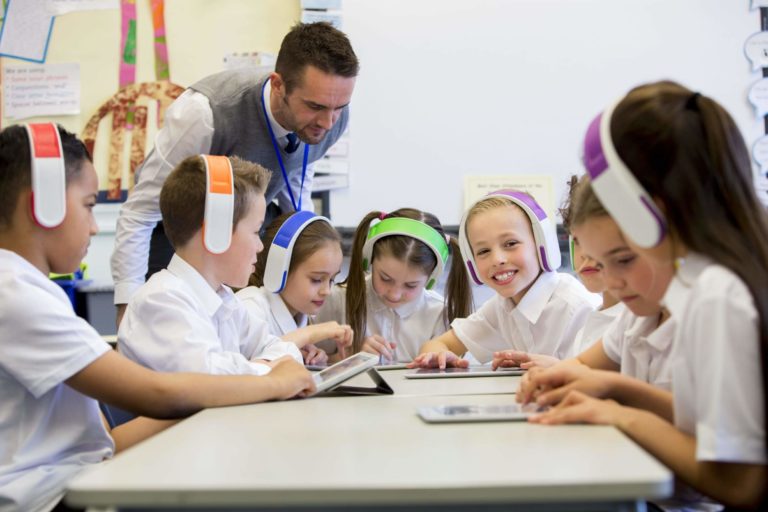 Group of young students wearing wireless headphones and using tablets in a classroom.