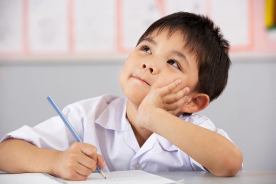 Young boy deep in thought while writing on paper