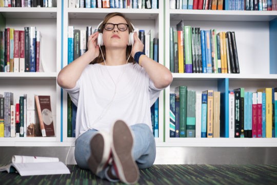 Female high school student sitting on the floor wearing headphones with her eyes closed