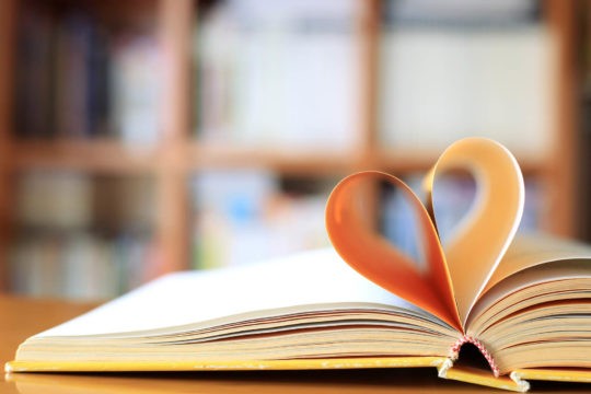 Open book on a desk with pages folded into a heart