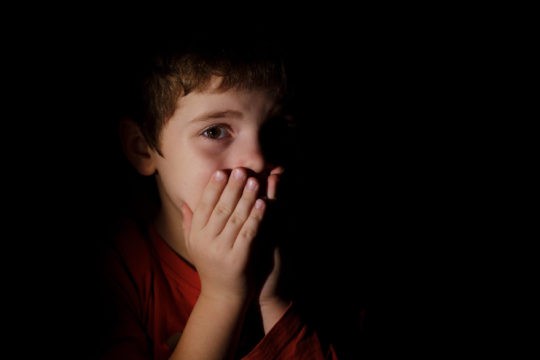 Young boy in the dark with hands over his mouth