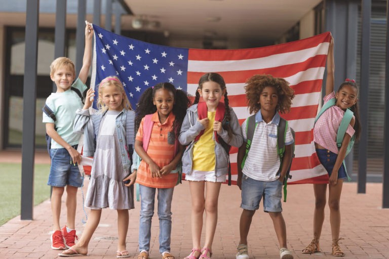 Group of young students with backpacks holding up an American flag.