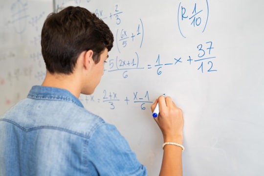 Male high school student working out equations on a white board