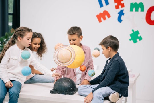 Group of young students looking at a solar system model.