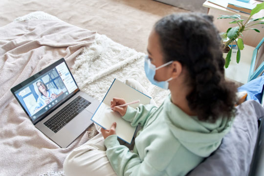 Young girl sitting in bed during a remote learning session.