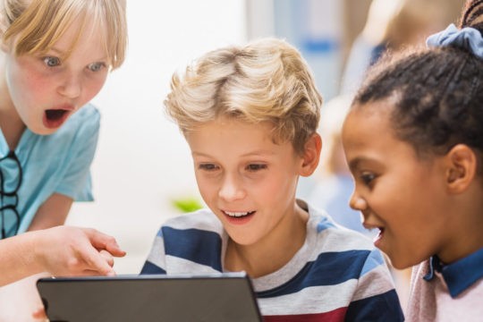 Two girls and boy excitedly use digital tablet computer in the classroom.
