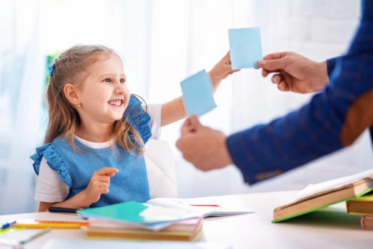 A girl chooses between two post-it notes that her teacher is showing her.