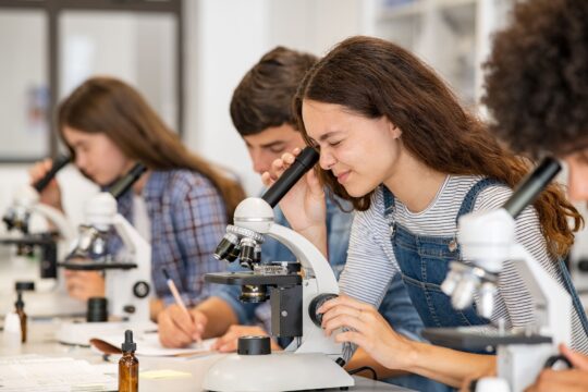 An older student uses a microscope in science class.